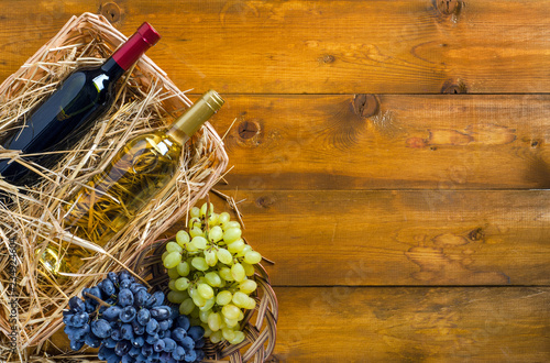 Two bottles with wine and grapes on wooden background.