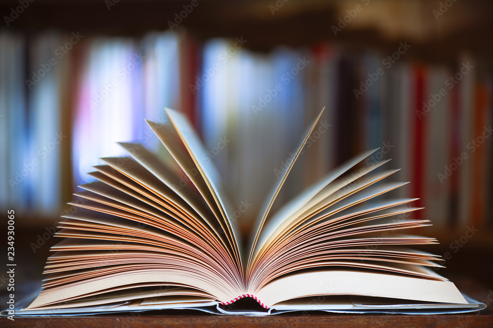 Fototapeta premium Open book with library background in the library