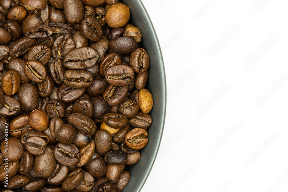 Closeup of lot of whole dark brown coffee beans sweet arabica variety in a grey ceramic bowl flatlay isolated on white background Closeup of lot of whole dark brown coffee beans sweet arabica variety in a grey ceramic bowl flatlay isolated on white background