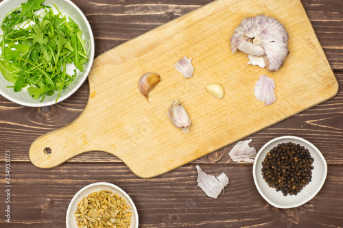 Peeling garlic cloves step. recipe step by step farfalle with arugula leaves on chopping board flatlay on brown wood