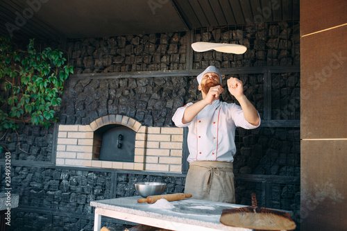 Tablou pe pânză Skilled chef preparing dough for pizza rolling with hands and throwing up