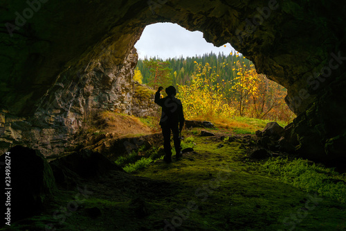 silhouette of a geologist examining a mineral sample found in a cave, on the background of an entrance with a brightly lit autumn forest