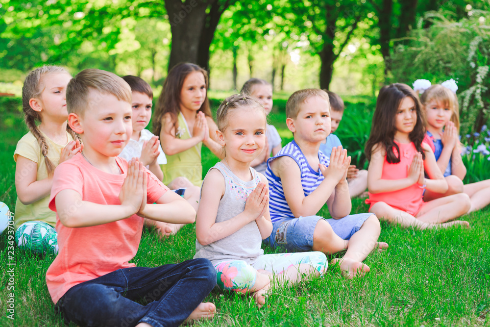 A large group of children engaged in yoga in the Park sitting on the grass. A large group of children engaged in yoga in the Park sitting on the grass.