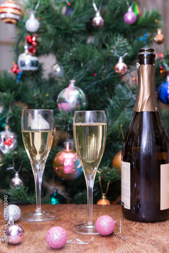 glasses of sparkling wine, a bottle of champagne, pink Christmas balls on the background of Christmas spruce