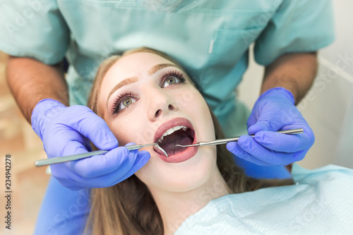 Close-up picture of young woman sitting in the dentist s chair with opened mouth at dentist s office while having examination.