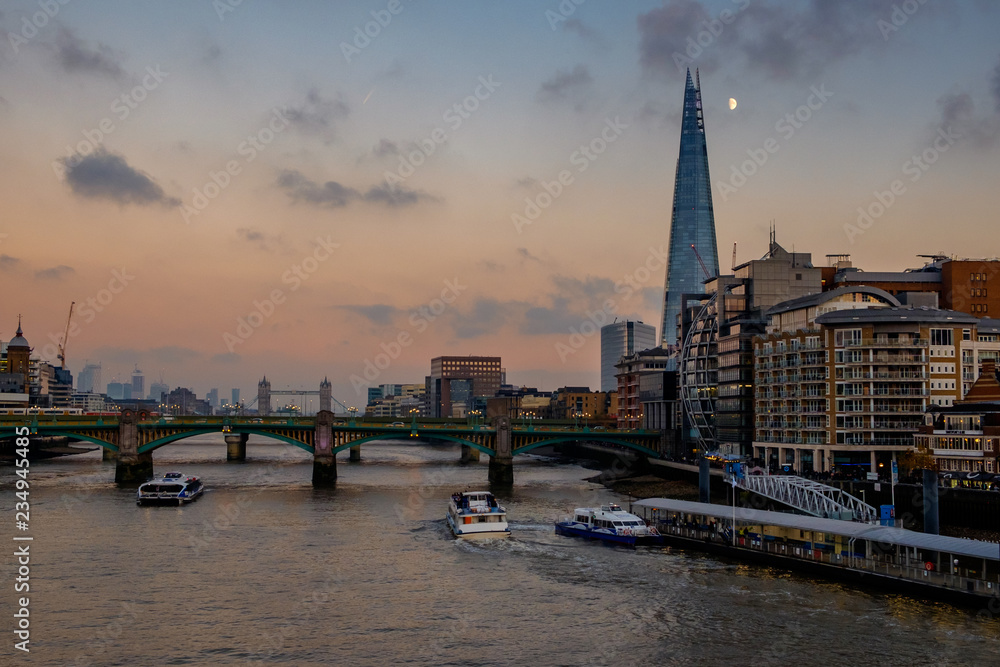 Sunset over the river Thames, London. The Shard building can be seen, with the moon to the side of it, high in the sky. 