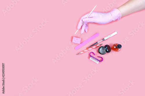 manicure and pedicure equipment. master nails in pink gloves holds manicure tool on the pink background. flat lay composition for card with a place for text