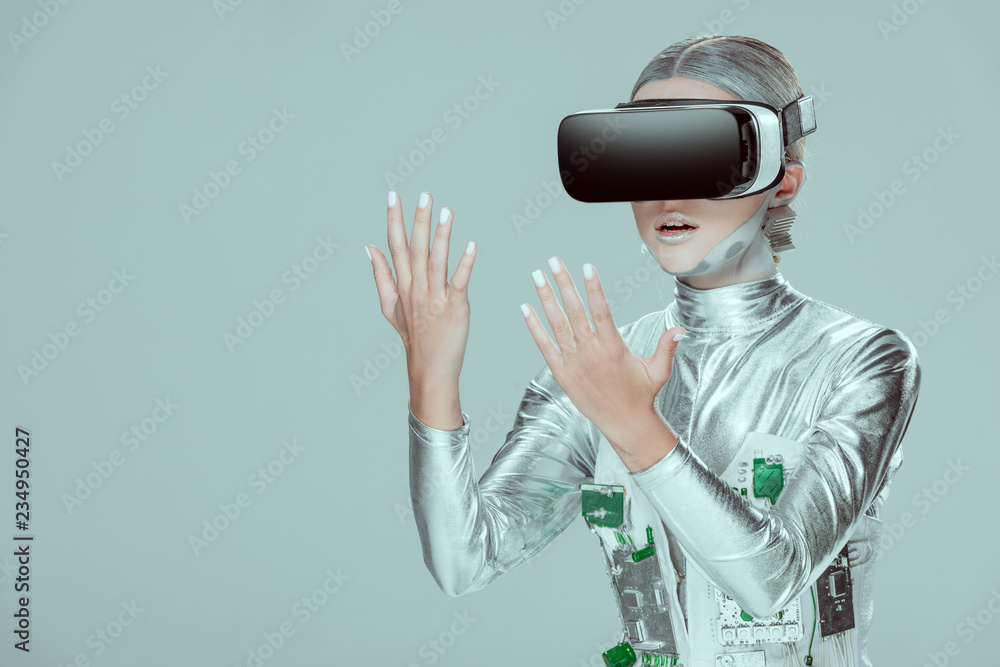 surprised silver robot looking at hands with virtual reality headset isolated on grey, future technology concept surprised silver robot looking at hands with virtual reality headset isolated on grey, future technology concept