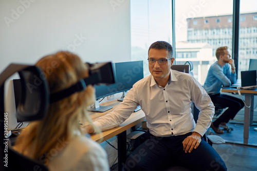 Man looking at woman wearing VR glasses in office photo