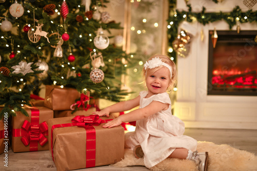 baby happiness little girl rejoices christmas under the tree fireplace and gifts