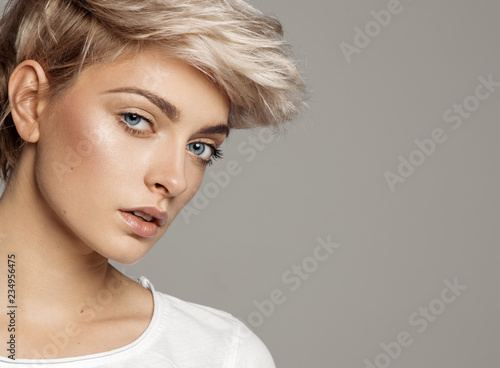 Portrait of young girl with blond short hairstyle looking at camera isolated on gray background with copy space