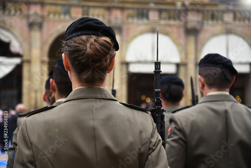 Detail with uniformed women standing during the military ceremony in Bologna, Italy. In the foreground, a woman seen from behind with a bayonet rifle.