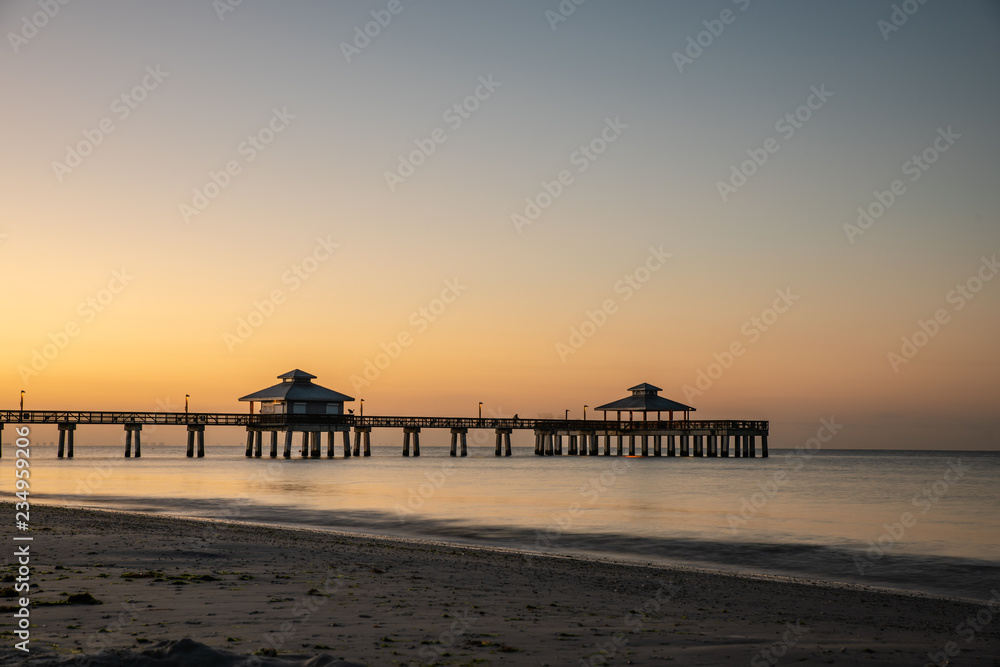 fort myers beach pier with flat water before sunrise, orange light at the horizon fort myers beach pier with flat water before sunrise, orange light at the horizon