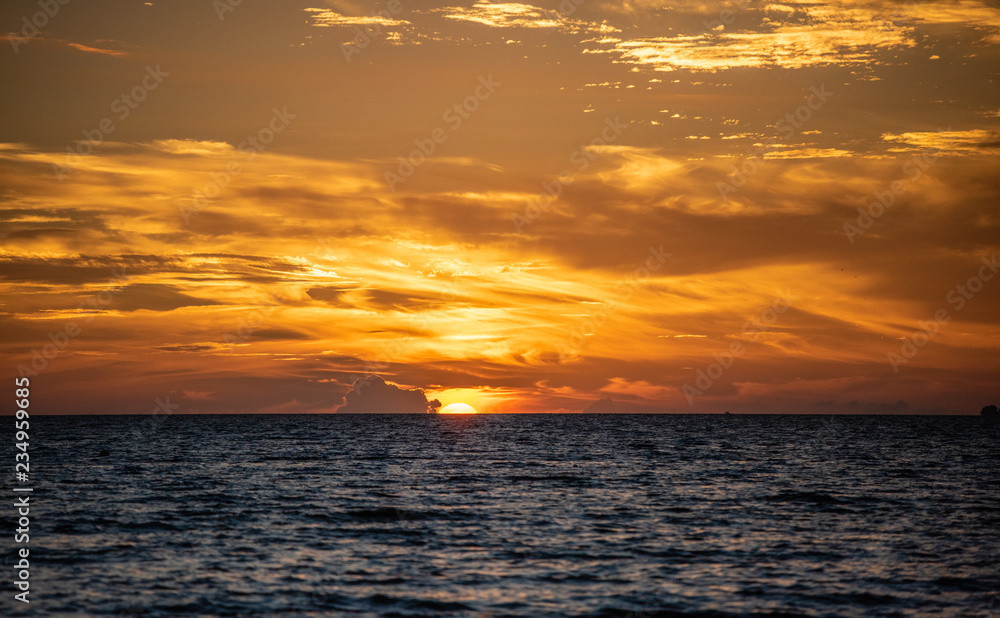 Obraz premium sunset over the sea, orange sun half in the water with sunlit clouds