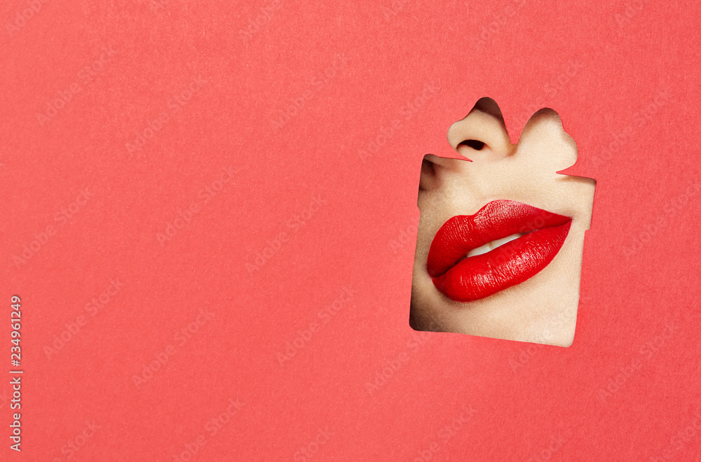 Obraz premium Beautiful Plump Bright Lips Of a Young Beautiful Woman with Red Lipstick Look Into the Pattern of Gift Box made of Colored Paper. Holiday Patterns. Red Paper