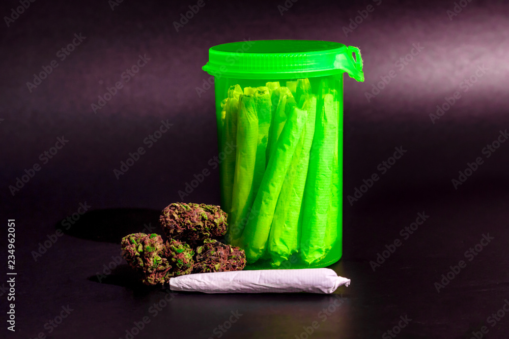 A bright transparent green RX pill bottle with marijuana joints inside next to a pile of dark marijuana and a joint