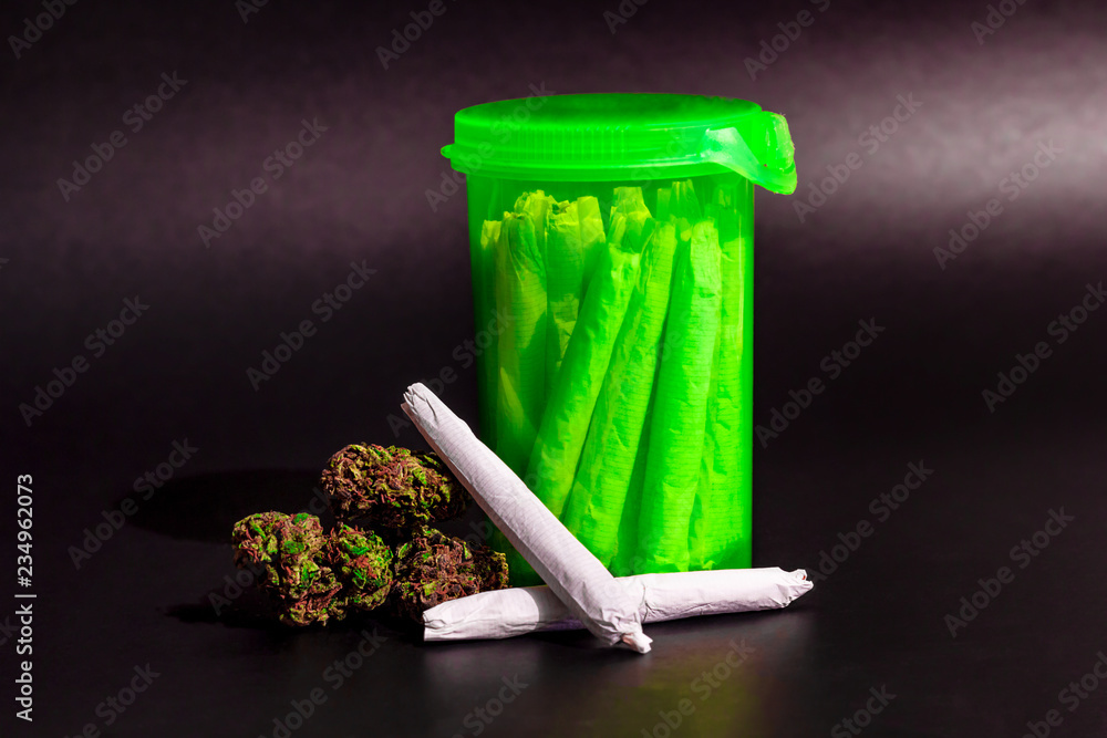 A bright transparent green RX pill bottle with marijuana joints inside next to a pile of dark marijuana and 2 joints