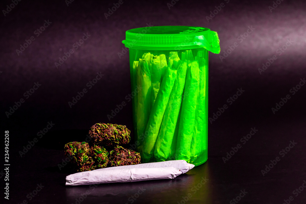 A bright transparent green RX pill bottle with marijuana joints inside next to a pile of dark marijuana and a joint