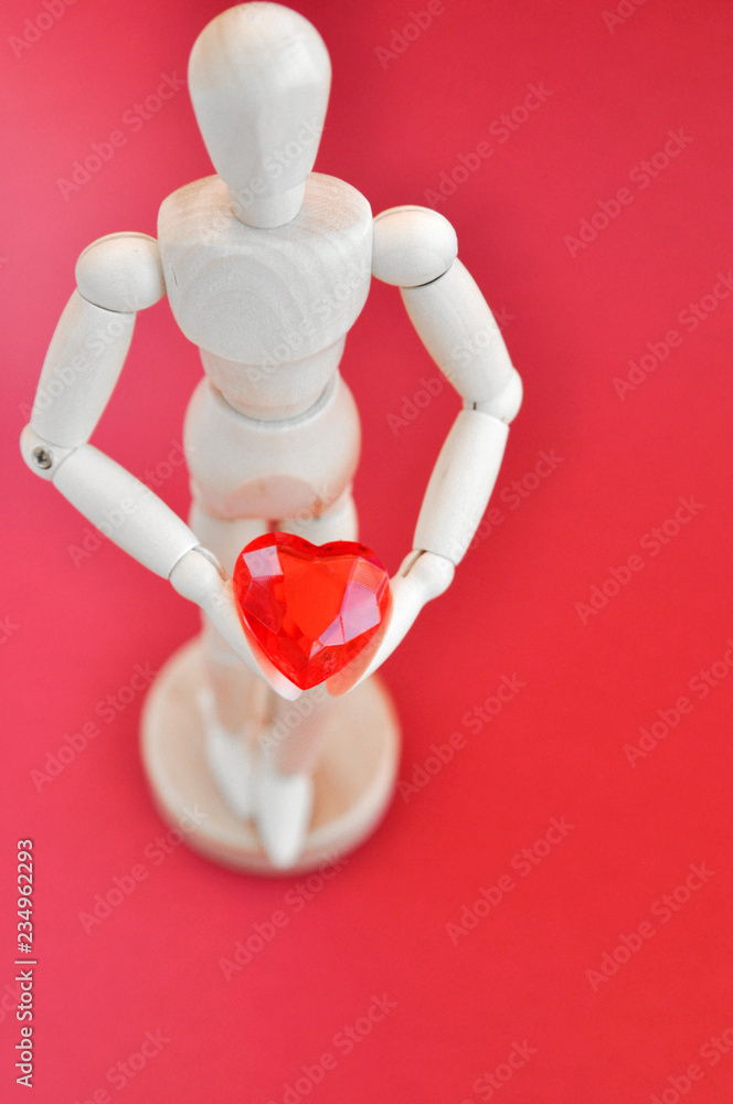 Bright concept for Valentine's day. Wooden model of a man holding a red heart on a red background. Bright concept for Valentine's day. Wooden model of a man holding a red heart on a red background.