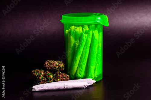 A bright transparent green RX pill bottle with marijuana joints inside next to a pile of dark marijuana and a joint
