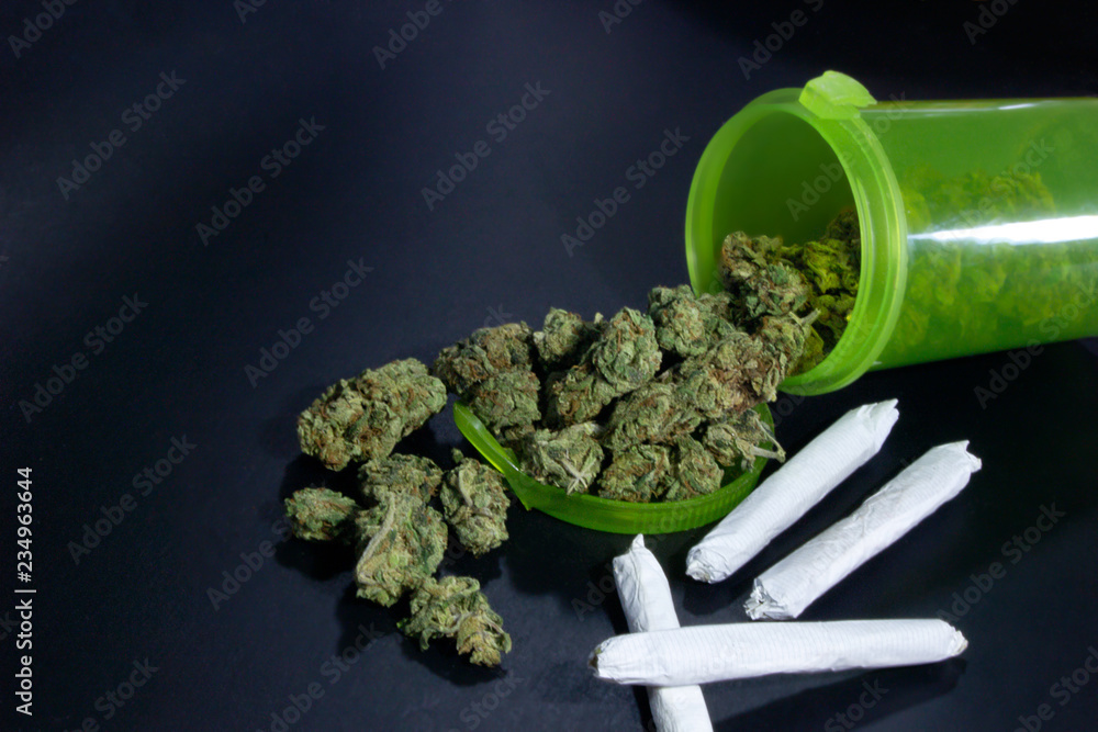 Close up of a bright green bill bottle full of marijuana buds spilling out next to 4 joints.