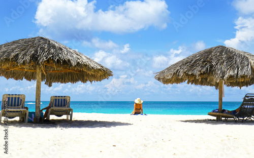 Cabana, parasol. White sand beach. Blue sea water and dramatic clouds. Oranjestad, Aruba. Famous Eagle Beach.  Unidentifiable sun bather. photo