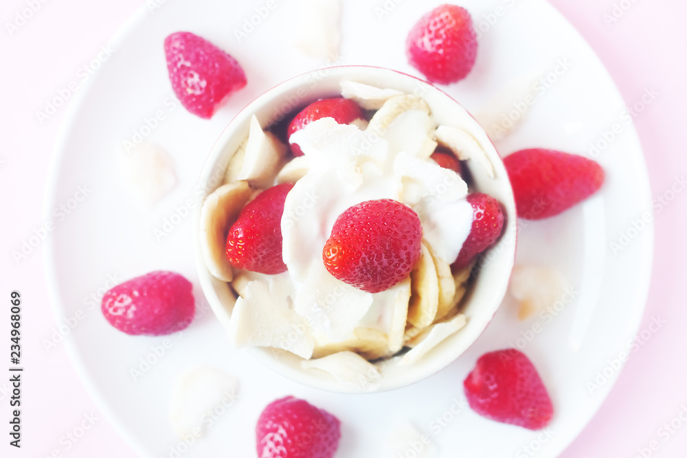 Healthy raw vegan dessert - banana and strawberry with coconut cream and coconut chips on pink background Healthy raw vegan dessert - banana and strawberry with coconut cream and coconut chips on pink background