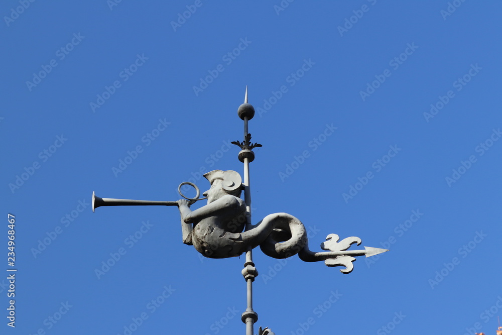 Rzeszow, Poland - 10 9 2018: Metal cast figure on the steeple of the town hall. The symbol of the urban community in the form of a human head with a snake tail blowing into the forge. Weathervane Rzeszow, Poland - 10 9 2018: Metal cast figure on the steeple of the town hall. The symbol of the urban community in the form of a human head with a snake tail blowing into the forge. Weathervane