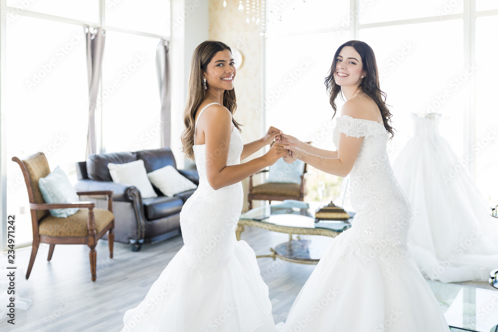 Female Buddies In Wedding Gowns Smiling In Store