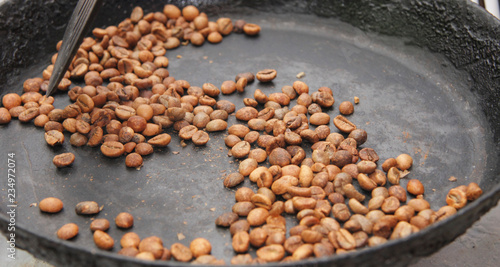 Green coffee beans roasting on the black pan