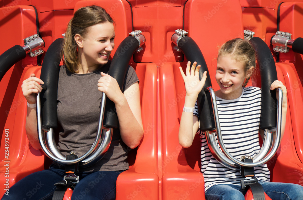 Mom and daughter are sitting on the attraction in the park. - obrazy, fototapety, plakaty 