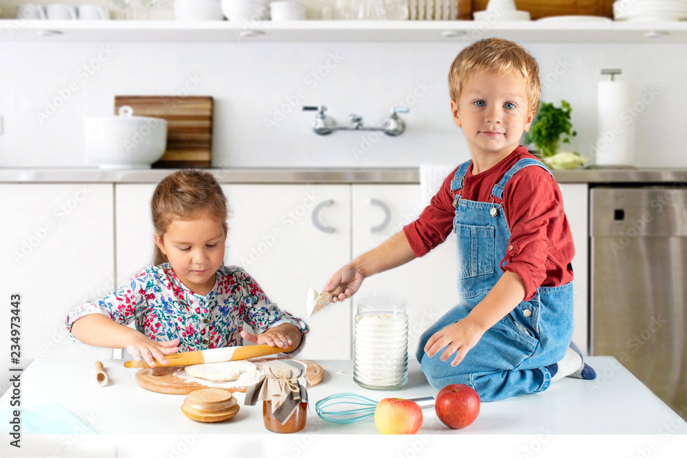 The little children, brother and sister, make a cake in the kitchen at home.