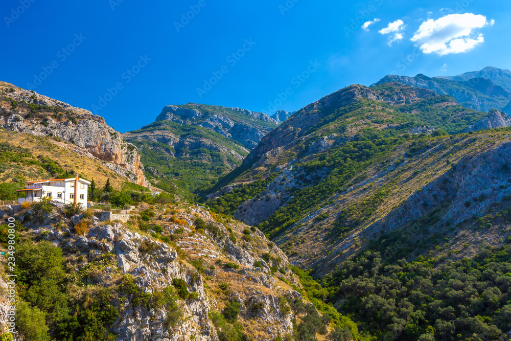 White house on the slope of a beautiful colorful mountain in front of the gorge opposite other side of the canyon on a sunny day with a blue sky. Summer landscape in Fortress Old Bar Town, Montenegro.