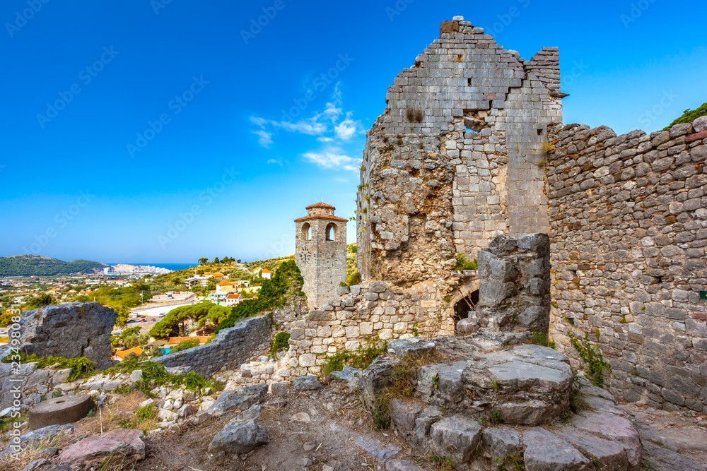 Renovated tower clock among ruined wall with crack of citadel in a sunny summer day and clear sky as postcard, copy-space for text. Summer landscape in Fortress Old Bar Town, Montenegro.