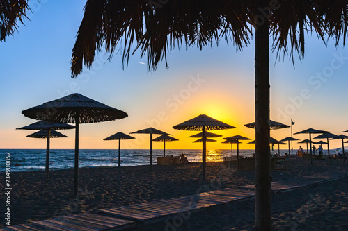 Sunset with colorful sun rays on the shore of the Adriatic Sea, paths sunbeds and umbrellas made of wood and straw in the recreation area on the sand. Beach on Ada Bojana, Ulcinj, Montenegro. photo