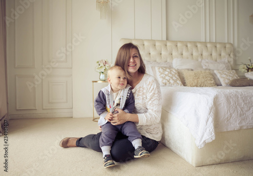 Loving young mother playing with her 1.5-year-old son in the bedroom. Happy mother holding and hugging her cute baby. The concept of a happy family lifestyle