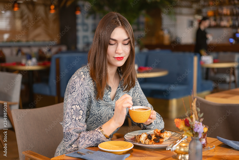 Young woman drinking coffee. Female holding cup. Sitting in coffee shop at wooden table. On table plate with breakfast. pleasant morning, the beginning of the working day