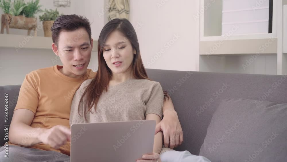 Asian couple using laptop for search web in living room at home, sweet couple enjoy love moment while lying on the sofa when relax at home. Lifestyle couple relax at home concept. Asian couple using laptop for search web in living room at home, sweet couple enjoy love moment while lying on the sofa when relax at home. Lifestyle couple relax at home concept.