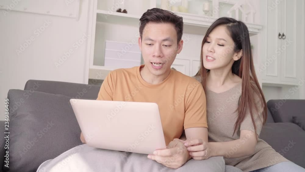 Asian couple using laptop for search web in living room at home, sweet couple enjoy love moment while lying on the sofa when relax at home. Lifestyle couple relax at home concept. Asian couple using laptop for search web in living room at home, sweet couple enjoy love moment while lying on the sofa when relax at home. Lifestyle couple relax at home concept.