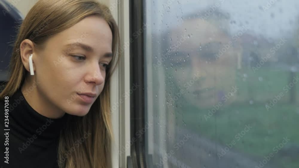 Woman with headphones in a bus train. Portrait of a woman passenger tourist. A woman listens aipods music headphones dreaming rainy day. Woman with headphones in a bus train. Portrait of a woman passenger tourist. A woman listens aipods music headphones dreaming rainy day.