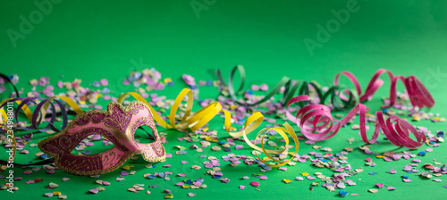 Carnival mask, streamers and confetti on bright green background