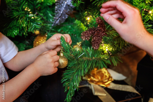 Close up baby hands decorating Christmas tree on Christmas eve at home. Young kid with winter decoration. Happy family at home. Christmas New Year december time for celebration concept