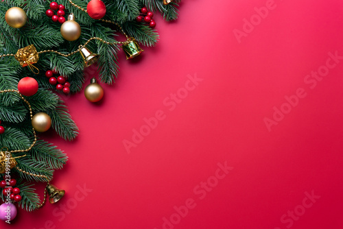 Christmas background concept. Top view of Christmas with spruce branches  pine cones  red berries and bell on red background.