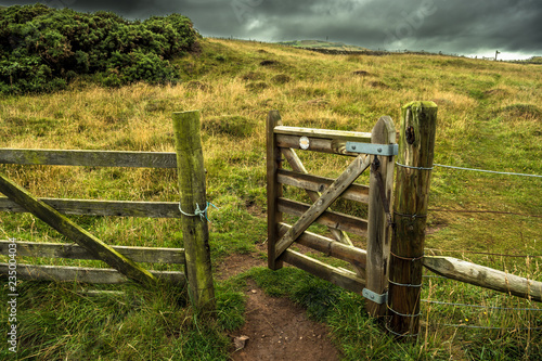 Open Wooden Gate In Fence With Rocky Trail To Grassy Pasture