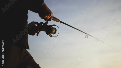 The hands of the fisherman twisting the coil on a fishing rod while catching predatory fish. Hands close up.