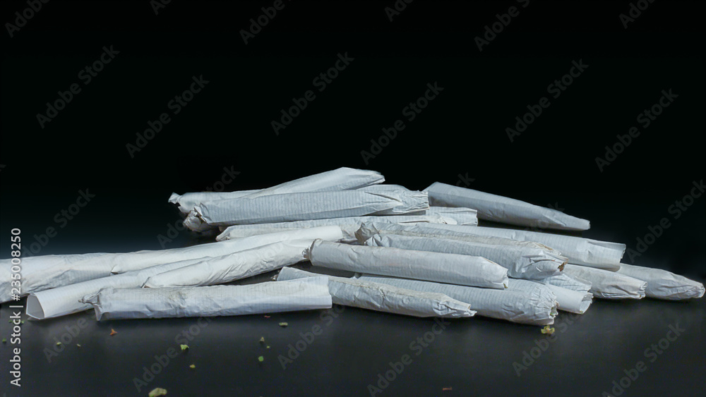Macro close up of a pile of marijuana joints ranging in size and thickness isolated on black.