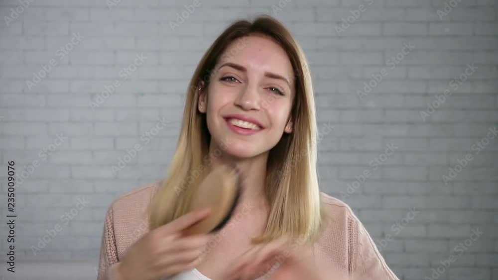 Beautiful young woman brushing hair while looking at camera 
