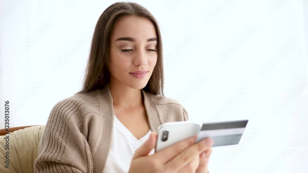 Young woman with credit card using smartphone indoors
