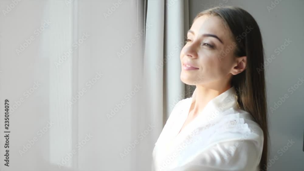 Young woman opening curtains at home on sunny morning
Young woman opening curtains at home on sunny morning