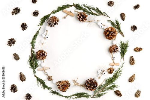 Christmas composition. A circle made with small branches of coniferous trees and christmas garland, and many pine cones around on a white background. Flat lay, top view, copy space